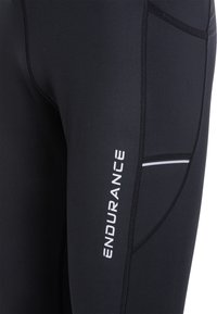 Svarta träningsleggings med platta sömmar, en sidoficka och en vit "ENDURANCE"-logotyp. Tyget verkar slätt och elastiskt.