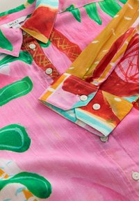 Chemise à col avec boutons, présentant un motif abstrait coloré en tons de rose, vert, rouge, jaune et bleu sur un tissu léger.