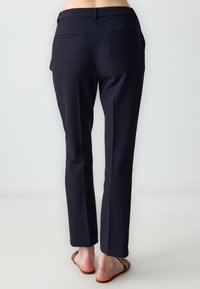 Marineblauwe taillepantalons met een rechte pijp, een gladde stof, twee achterzakken en een riemlusdetail, gecombineerd met platte sandalen.