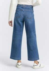 Jeans in denim blu a gamba larga con vita alta, due tasche posteriori e una linea dritta dalla vita all'orlo. Abbinati a sneakers bianche.