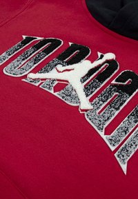 Felpa rossa con logo "JORDAN" in rilievo e ricamato in bianco e nero, che presenta la silhouette di una figura che salta.