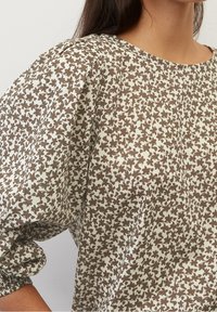 Blusa a fiori marrone con vestibilità ampia, scollo rotondo e maniche a sbuffo, realizzata in tessuto leggero con una texture morbida.