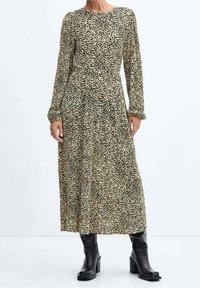 Robe à manches longues, longueur genou, avec un motif à pois vert et crème. Fabriquée en tissu léger, avec un col rond et des poignets élastiques. Bottes à talons noires.