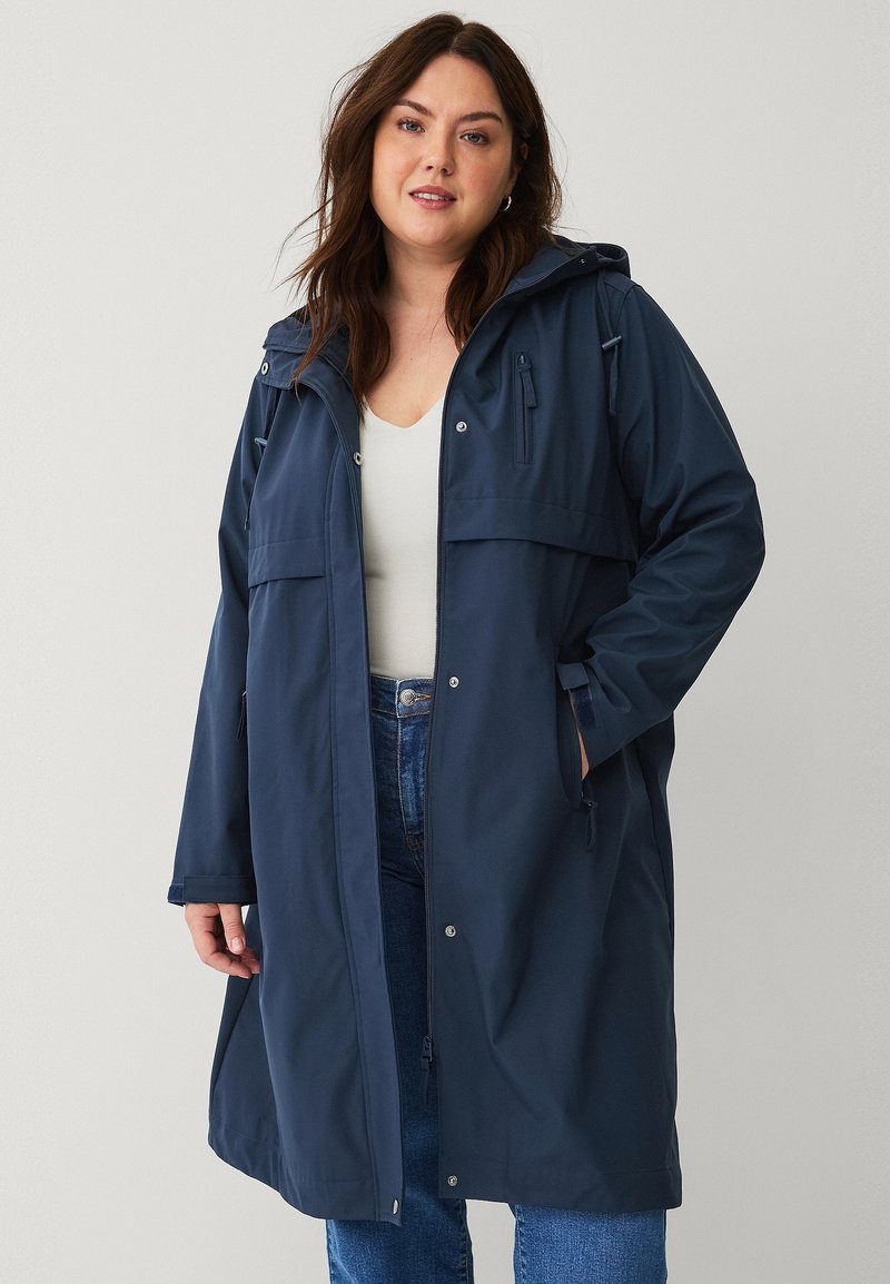 Navy waterdichte parka met een capuchon, front rits, drukknoopsluiting, twee grote zakken en verstelbare koordjes in de taille en aan de onderkant.