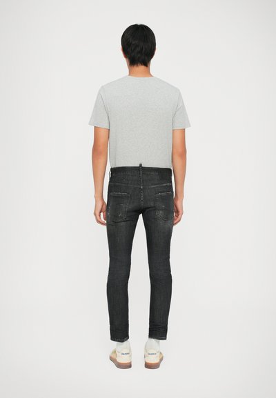 Camiseta gris de manga corta combinada con jeans ajustados negros, con una textura desgastada, bolsillos traseros y zapatillas blancas con suelas de color claro.