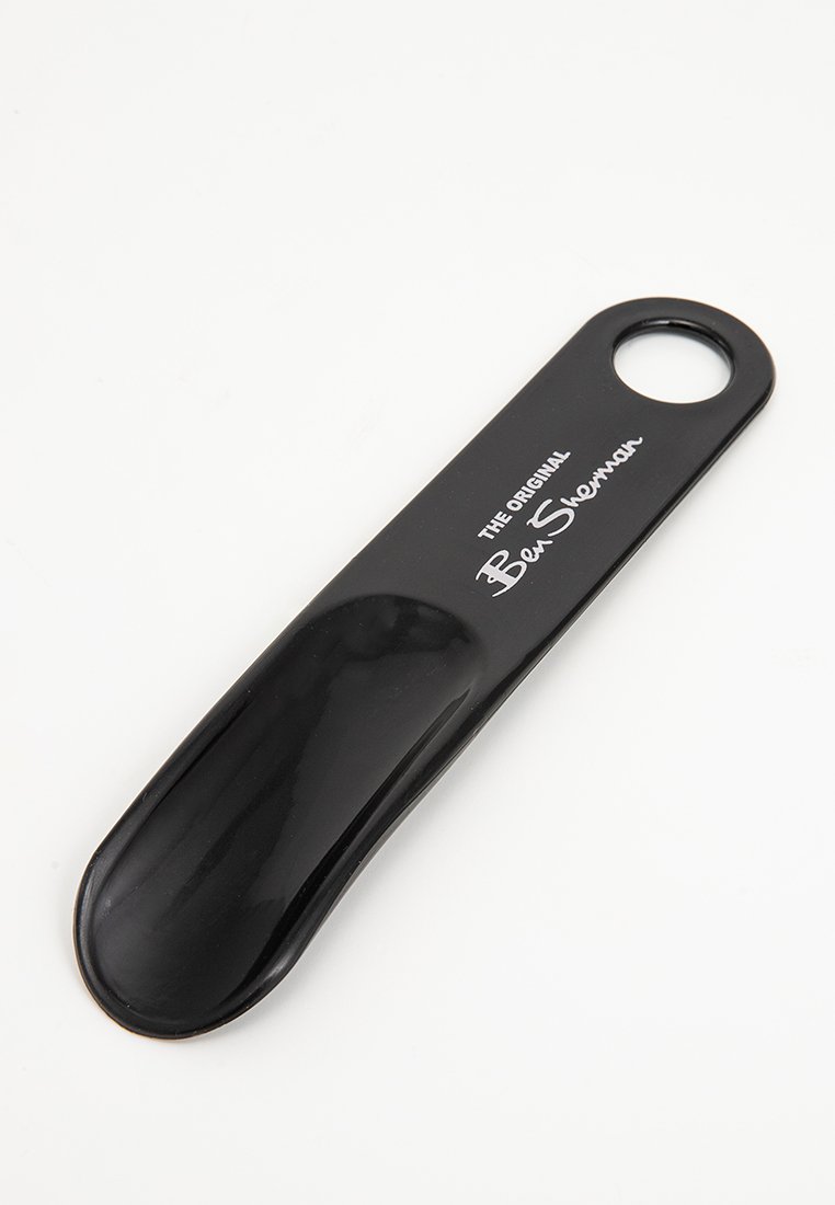 Chausson en plastique noir avec une poignée arrondie comportant un trou pour le suspendre et le texte "The Original Ben Sherman" en blanc.