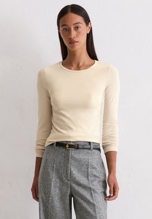 Beige langemouwige aansluitende top met een ronde halslijn, gecombineerd met hoog-waist grijze gestructureerde broeken en een zwarte riem met een gouden gesp.