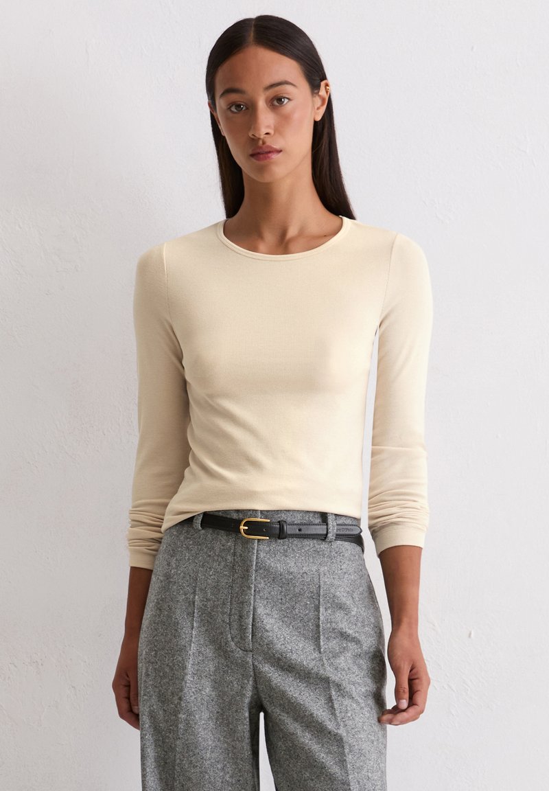 Beige langemouwige aansluitende top met een ronde halslijn, gecombineerd met hoog-waist grijze gestructureerde broeken en een zwarte riem met een gouden gesp.