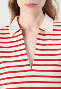 Červeno-bílý pruhovaný polo tričko s designem do V a kontrastním pevným límečkem. Vyrobeno z měkké tkaniny, která předvádí čistý, ležérní vzhled.