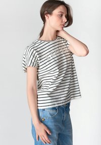 Camiseta de manga corta a rayas en blanco y negro con cuello redondo y el texto "CEREBEL" adornado con tachuelas; combinada con vaqueros de tiro alto azul.