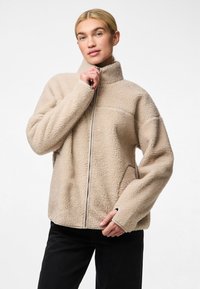 Jachetă din fleece bej cu guler înalt, fermoar anterior și buzunare laterale. Textură moale, umeri lăsați și detaliu de fermoar contrastant.