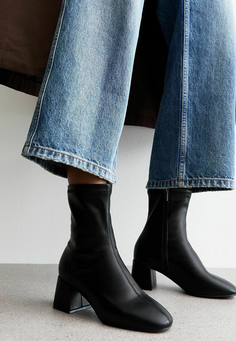 Botines negros de piel suave con punta cuadrada y tacón ancho. Combinados con unos vaqueros de pierna ancha en un tono azul claro.
