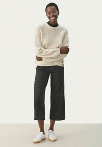 Fyldig creamfarvet strikket sweater med ribbet kant, parret med sorte ternede cropped bukser og hvide sneakers med gummisål.