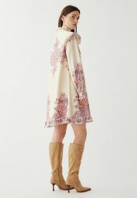 Langærmet, cremefarvet kjole med pink og blå paisley-mønster, flæset krave og kant. Båret med knæhøje beige ruskind støvler.