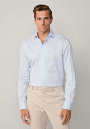 Chemise bleu clair à manches longues en tissu lisse, dotée d'un col pointu et d'une fermeture à boutons, assortie à un pantalon beige.