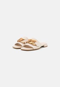 Beige öppna tå-mules med en bred rem och en guldkedja på överdelen. Låga blockklackar och mjuk textur.
