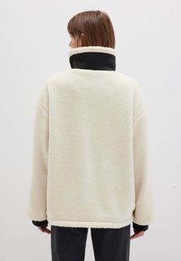 Fleece-Pullover in Creme mit hohem schwarzen Kragen. Hat eine strukturierte Oberfläche und entspannte Passform, mit langen Ärmeln und geradem Saum.