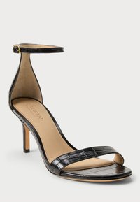 Μαύρη λουστρινένια σαμπό με τακούνι, που περιλαμβάνει λεπτή λουρί στον αστράγαλο, ανοιχτό μπροστινό σχέδιο και υφή από κροκοδειλίσια επιδερμίδα στην πάνω πλευρά.