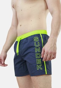 Shorts da bagno navy con dettagli verde neon e cordoncino. Materiale leggero con una texture liscia. Logo stampato di lato.