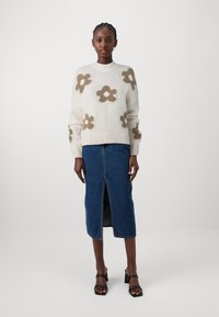 Maglione a maglia color crema con motivo floreale marrone, abbinato a una gonna midi in denim con spacco frontale e sandali neri con tacco.