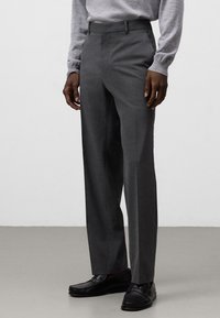 Pantaloni grigi su misura con un design a gamba dritta, realizzati in tessuto strutturato. Presentano passanti per cintura e tasche laterali, abbinati a mocassini neri.
