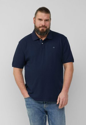 Marineblaue Baumwollpoloshirt mit Kragen und einer Drei-Knopf-Leiste, kurzärmlig und mit kleinem Logo auf der Brust. Getragen mit Jeans.
