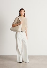 Megztinis smėlio spalvos, derinamas su baltais plačiomis kelnėmis ir kreminės spalvos pečių rankine. Lygūs audiniai, laisvas siluetas ir minimalistinis dizainas.