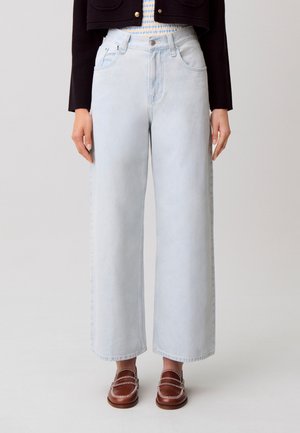 Jean large bleu clair porté avec des mocassins marron et une veste courte noire sur un haut rayé, vu de la taille aux pieds.