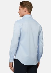 Svetlo modrá košeľa s dlhým rukávom a klasickým golierom, zakriveným lemom a zapínaním na gombíky, vyrobená z hladkej tkaniny s minimálnou textúrou.