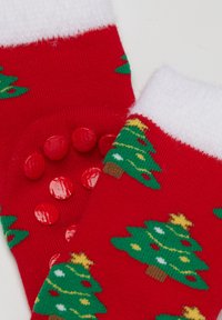 Red socks with a white fuzzy cuff, featuring green Christmas trees and yellow stars, and red rubber grips on the bottom for traction.