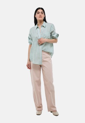 Chemise surdimensionnée rayée verte et blanche avec un design à boutons, associée à un pantalon large rose clair et des chaussures de couleur neutre.