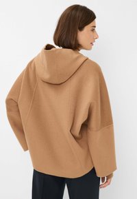 Bruine oversized hoodie van een zachte, gestructureerde stof, met een capuchon, verlaagde schouders en een ontspannen pasvorm. Minimalistisch ontwerp en steekdetails.