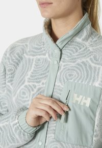 Jasnoniebieska polarowa kurtka z teksturowanym, spiralnym wzorem, z zapięciem na napy, elastycznymi mankietami i zamykana kieszenią na klatce piersiowej z logo.