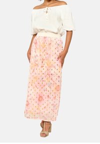 Jupe longue et fluide en tissu rose doux ornée de motifs floraux et d'accents métalliques dorés. Assortie à un haut clair à épaules dénudées.