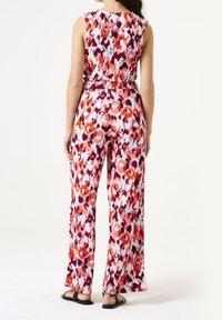 Kombinezon w wzory z kwiatowym motywem w odcieniach różu, pomarańczy i fioletu. Posiada szerokie nogawki i pasek w talii. Wykonany z lekkiego materiału.