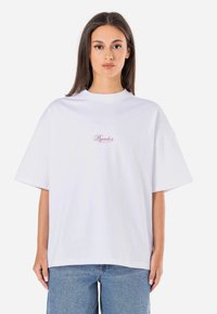 White oversized t-shirt made of cotton, featuring short sleeves and a round neck. It has red embroidered text on the front.