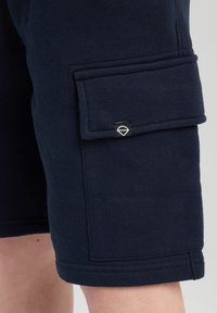 Navy blue cargo shorts made from soft fabric. Features a side pocket with a decorative metal accent and a stitched hem.