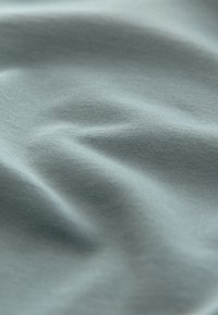 Hellblauer Stoff mit feiner gerippter Textur und weichen Falten, die subtile Schatten und Lichtreflexe erzeugen.