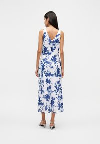 Μακρύ floral φόρεμα χωρίς μανίκια με μπλε και λευκό χρωματικό συνδυασμό, σχέδιο με V στην πλάτη και αέρινη σιλουέτα.