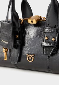 Svart skinnhåndveske med gullhardware, en lås, to stropper og et dekorativt logo med insektmotiver. Jevn tekstur med en blank overflate.