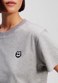 Grijze katoenen t-shirt met een ronde hals, met een zwart-wit geborduurde kattenpatch met een zonnebril op de borst.