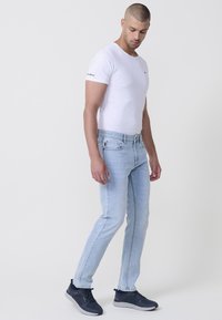 Jeans de denim azul claro con un corte ajustado, combinados con una camiseta blanca entallada y zapatillas oscuras. La camiseta presenta un pequeño logo en la manga.