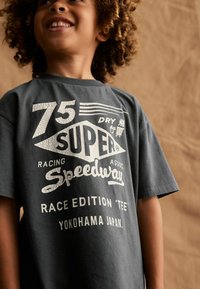 Grå bomulds t-shirt med hvidt vintage-stil grafisk tekst: "75 SUPER SPEEDWAY RACING ASSOC." Korte ærmer og afslappet pasform.