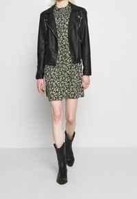 Svart läderbikerjacka över en blommönstrad svart klänning med korta ärmar, i kombination med knähöga svarta cowboystövlar.