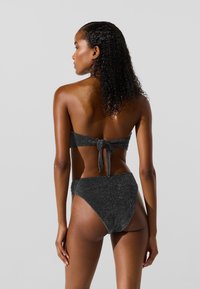 Black glitter bikini set featuring a bandeau top with a tie back and high-waisted bottom; smooth texture with a shimmer effect.