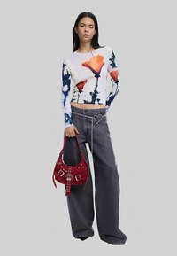 Long-sleeve cropped top with floral design in orange and blue, paired with grey wide-leg jeans and a red suede handbag featuring studs.