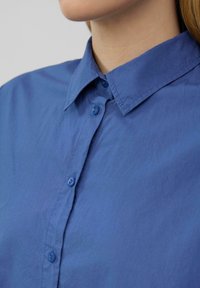 Blauw overhemd met knoopsluiting, gemaakt van gladde stof. Kenmerkt zich door een klassieke snit en een platte kraag. De textuur lijkt licht gekreukt.