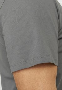 Grå bomulds T-shirt med rund hals, korte ærmer og en glat tekstur. Sømmen er syet med en subtil finish.