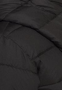 Tessuto nero trapuntato con cuciture imbottite che formano grandi sezioni rettangolari morbide, probabilmente parte di una giacca o cappotto invernale.