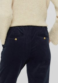 Navy Cordhosen mit entspannter Passform, ausgestattet mit zwei Gesäßtaschen mit goldfarbenen Knopfakzenten und einem weichen, strukturierten Stoff.